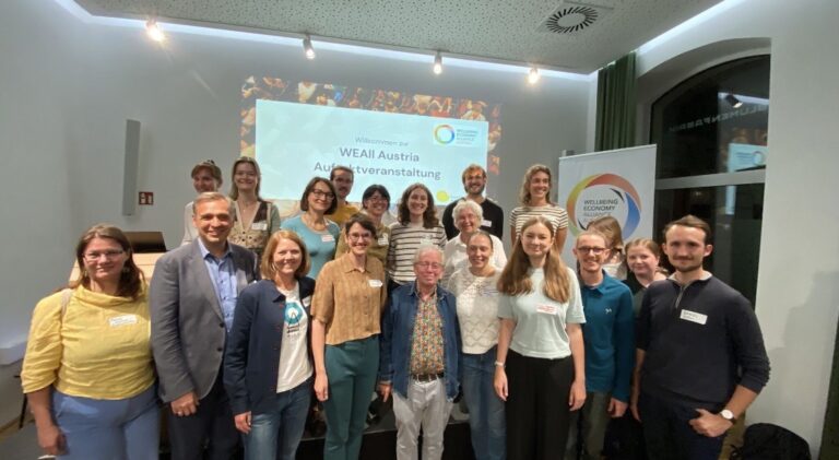 etwa 30 Menschen stehen lächelnd vor einer Leinwand auf der steht WEAll Austria Auftaktevent